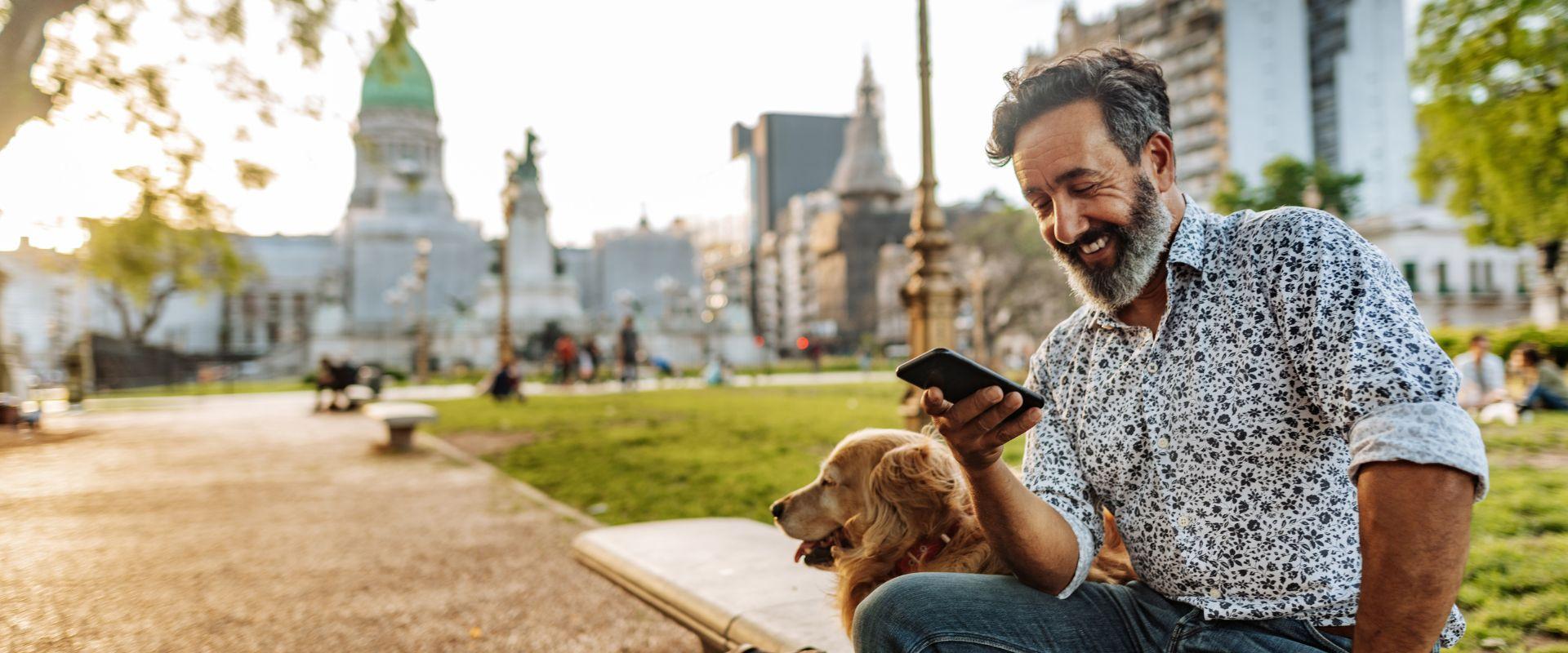 Hombre sentado en un parque con su perro mirando su teléfono