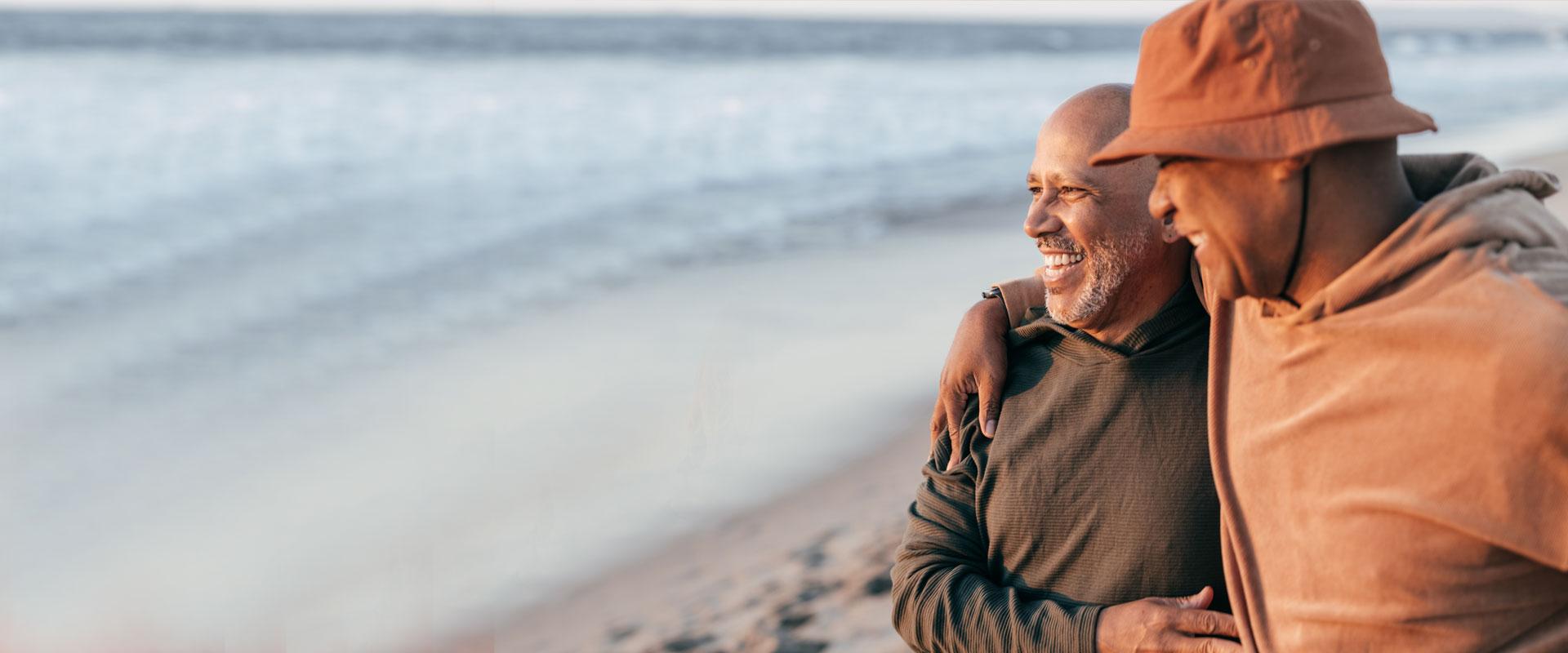 Two men on the beach hug each other as they look over the ocean