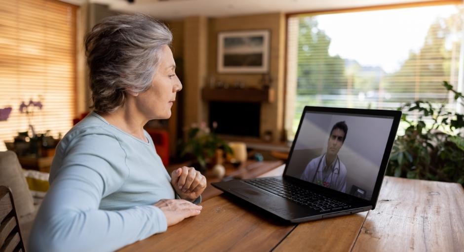 Woman having a telemedicine appointment with her doctor via a laptop in her dining room