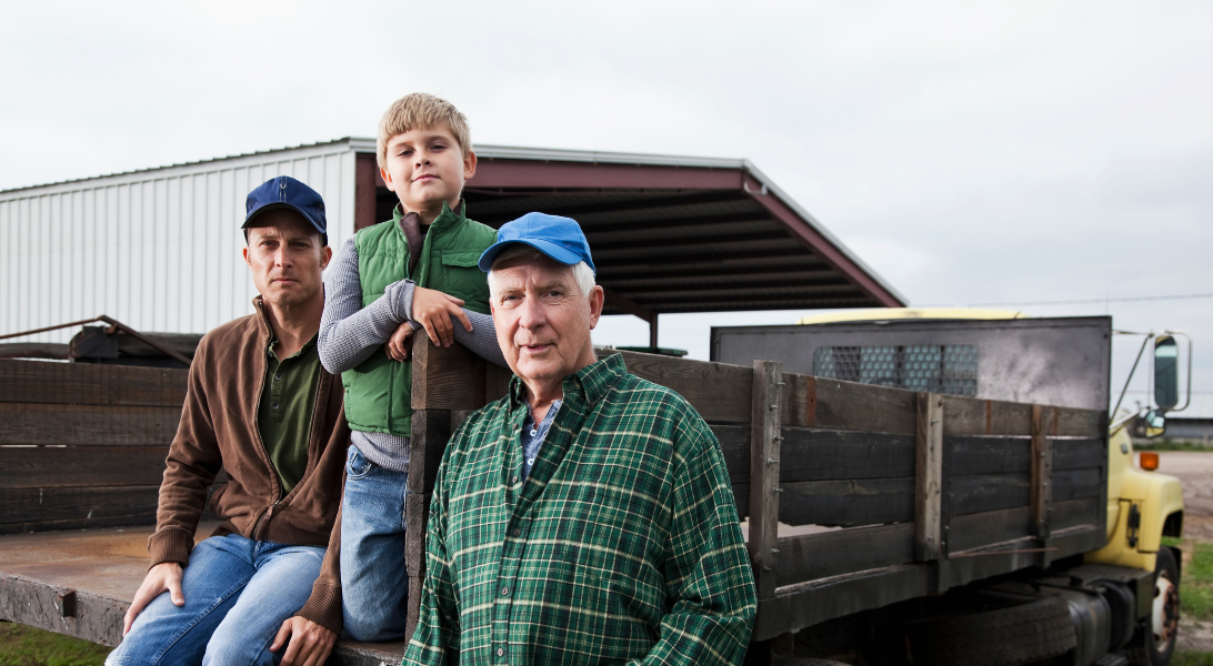 Three generations of male farmers sitting on the back of a truck