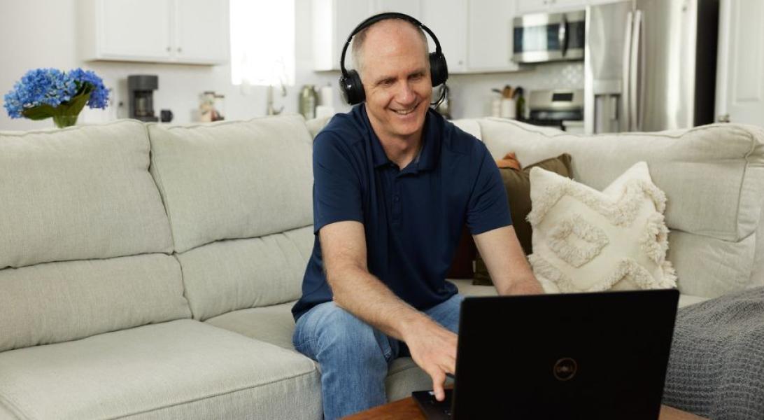 Man sitting on the couch with headphones on looking at a laptop