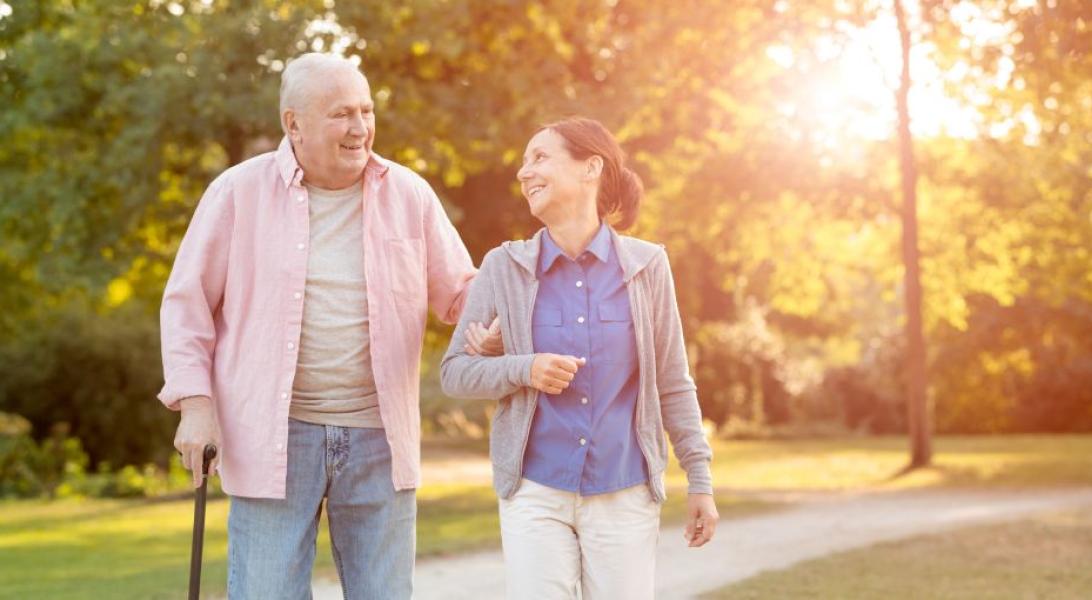 A younger woman walking with an older man, holding a cane