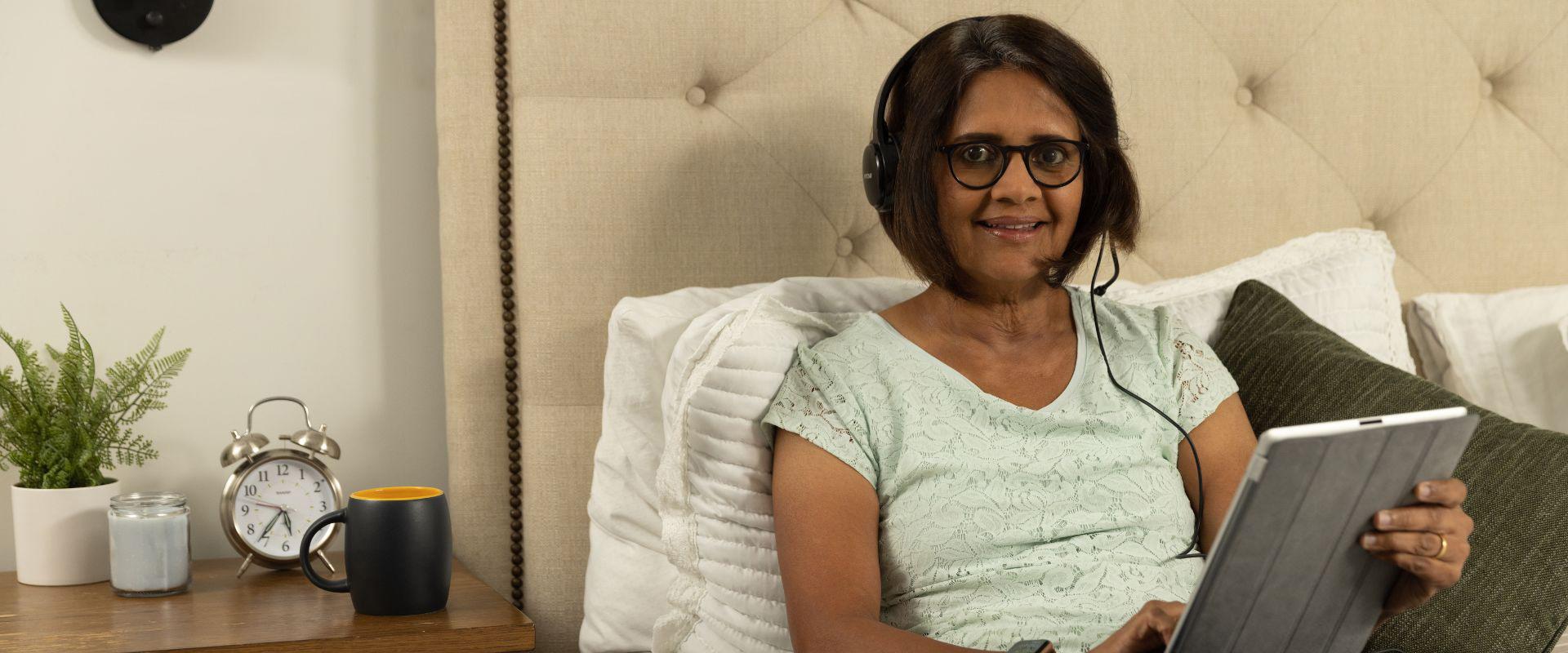 Woman sitting in bed on her tablet with headphones on