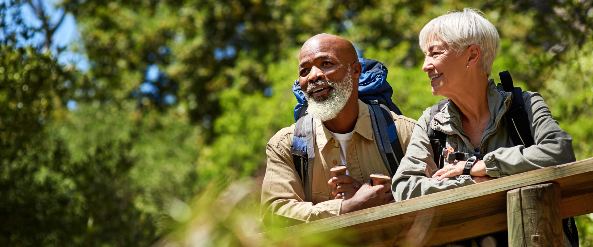 A black man and an Asian woman look over the railing of a trail boardwalk on a beautiful and sunny summer day
