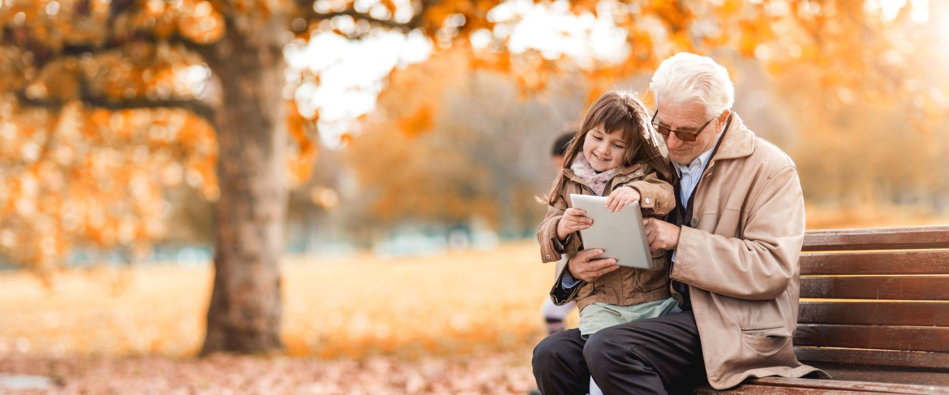 Man sitting in the park with his granddaughter and teaching her how to use touchpad.