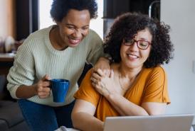 Two women holding hands, looking at a laptop