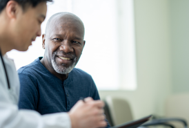 An older man smiles while talking with a doctor during a medical consultation.