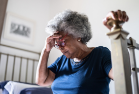 Woman sitting on bed holding head because she's feeling dizzy