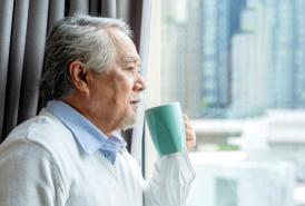 Asian man looking out the window while drinking coffee