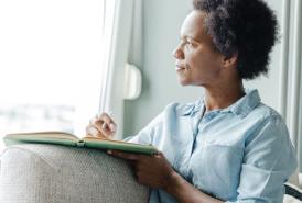 Woman looking out the window while writing in a notebook