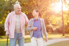 A younger woman walking with an older man, holding a cane
