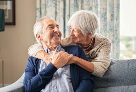 Wife with her arms wrapped around her husband sitting on the couch