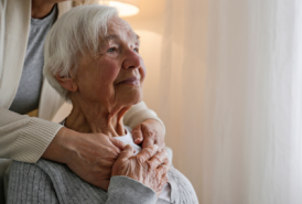 an elderly mother looking off in the distance while being hugged by her daughter not in the frame