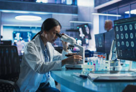female scientist viewing a slide under a microscope in lab setting