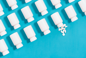 White pill bottles arranged in an organized fashion on a blue background with one bottle spilling pills