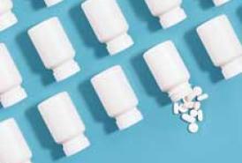 White pill bottles arranged in an organized fashion on a blue background with one bottle spilling pills