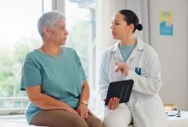 A female patient talking with her doctor who is holding a tablet.