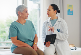A female patient talking with her doctor who is holding a tablet.