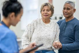 La paciente se sienta en la camilla de exploración con su marido cerca.