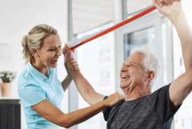 Man using resistance band above head while physical therapists assists