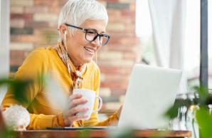 Woman looking at laptop with headphones in while drinking coffee