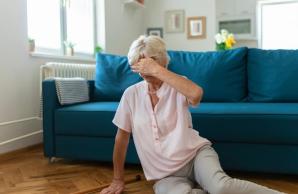 Woman sitting on floor in front of couch with left hand over eyes, indicating dizziness