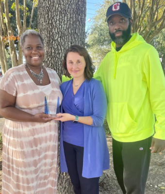 Kelly Spain holding award with two people