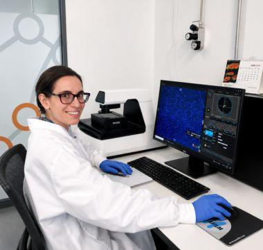 Nora seated at a computer workstation in a research lab.