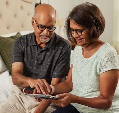 Radhika and Dharma sitting on bed looking at tablet