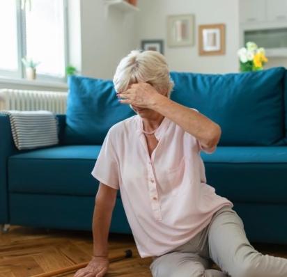 Woman sitting on floor in front of couch with left hand over eyes, indicating dizziness