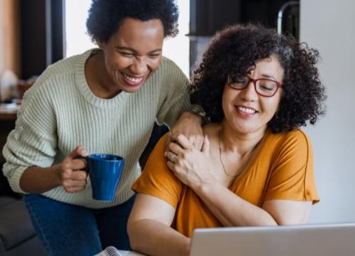 Two women holding hands, looking at a laptop