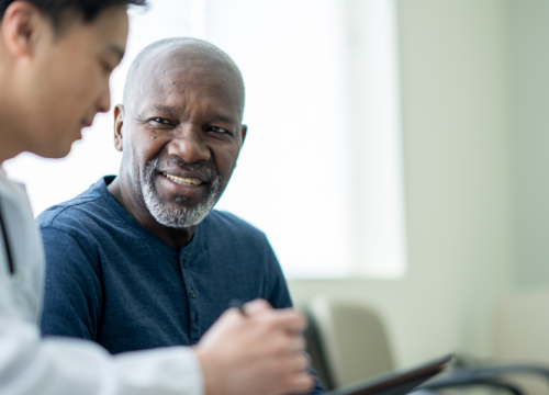 An older man smiles while talking with a doctor during a medical consultation.
