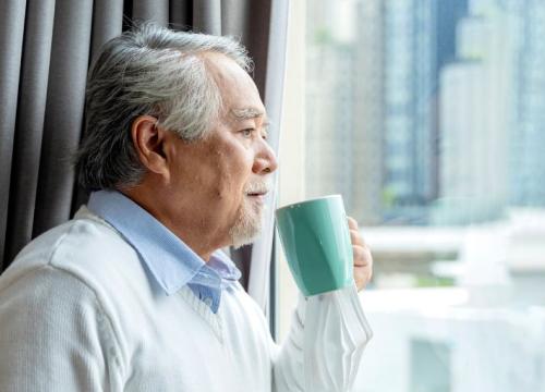 Asian man looking out the window while drinking coffee