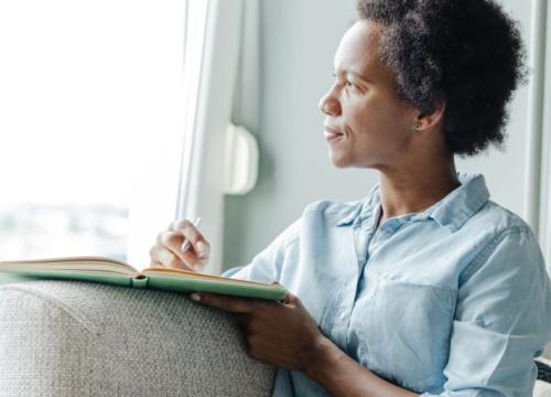 Woman looking out the window while writing in a notebook