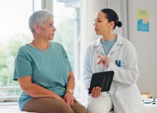 A female patient talking with her doctor who is holding a tablet.