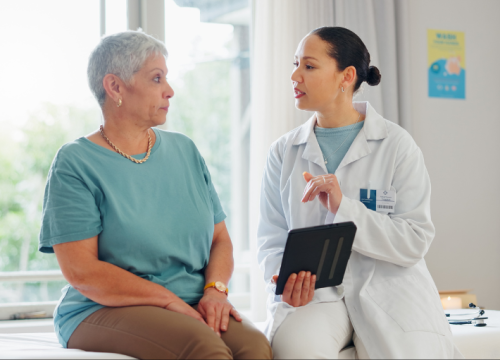 A female patient talking with her doctor who is holding a tablet.