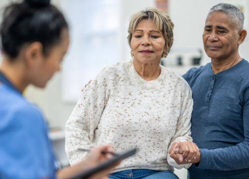 La paciente se sienta en la camilla de exploración con su marido cerca.
