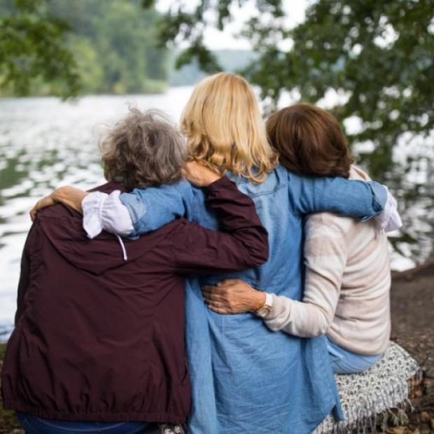 Three women sitting on a bench by a lake hugging