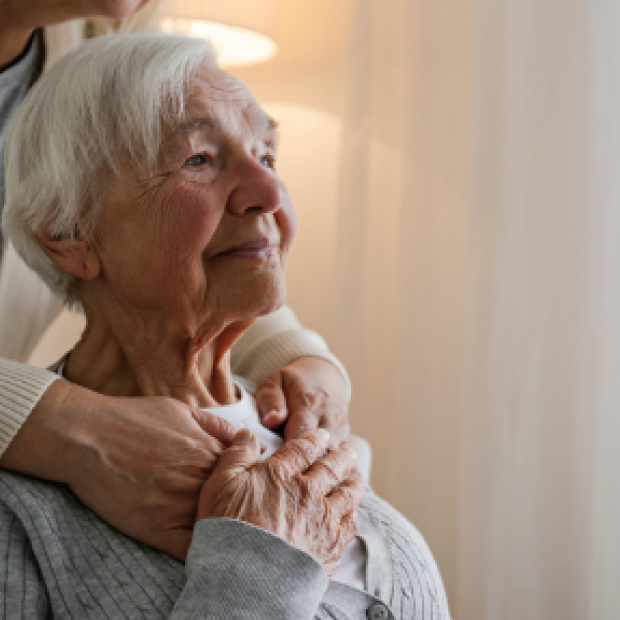an elderly mother looking off in the distance while being hugged by her daughter not in the frame