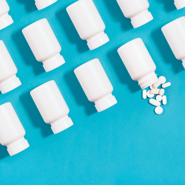 White pill bottles arranged in an organized fashion on a blue background with one bottle spilling pills
