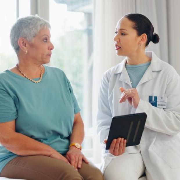A female patient talking with her doctor who is holding a tablet.