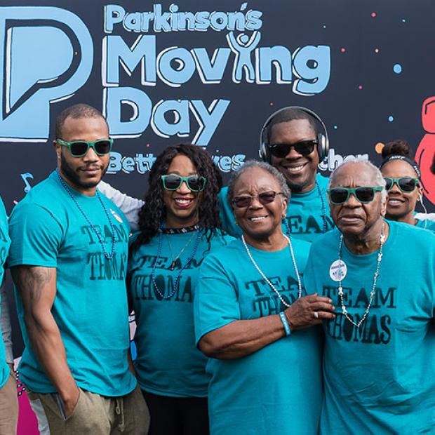Moving Day banner - Multigenerational family standing in front of a hand-drawn Moving Day logo at the Parkinson's Foundation walk