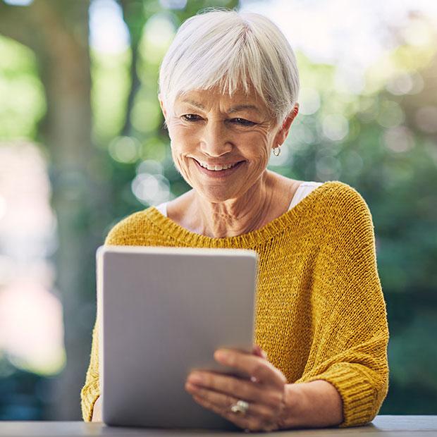 Older woman sitting outside engages with a tablet