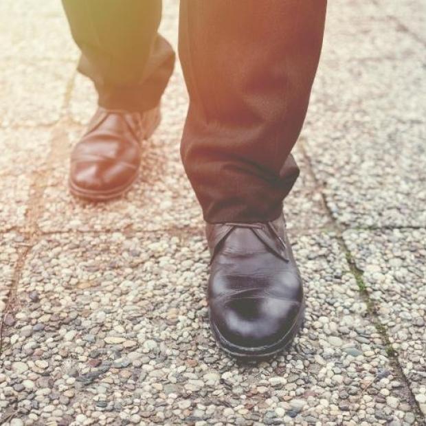 Man's feet and legs walking on sidewalk with assistance from a cane