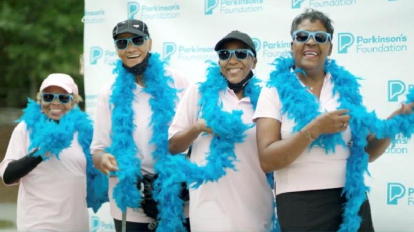 Screenshot from the Moving Day PSA where four women pose wearing blue feather boas, having fun