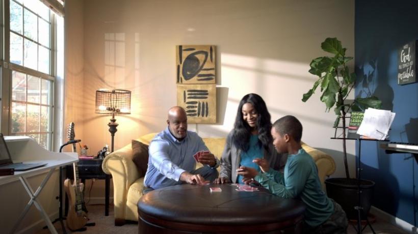 Screenshot of PSA where three members of a family sit around a table playing cards together.