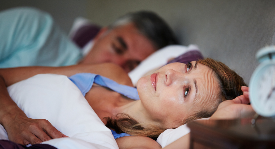 Woman laying in bed restless while husband sleeps next to her