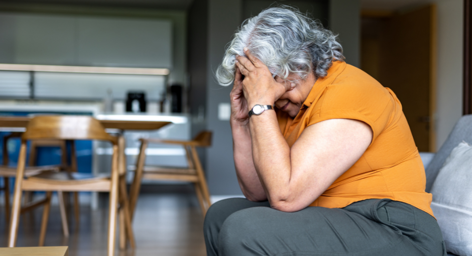 Elderly woman sitting down with head in her hands.