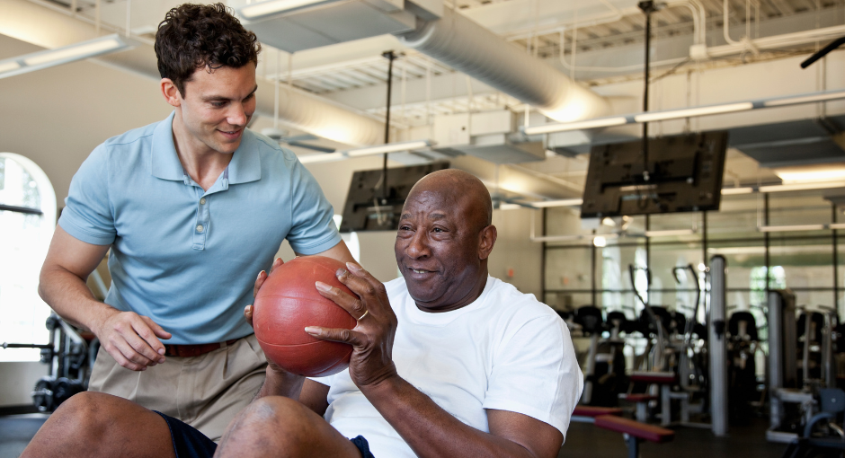 Personal trainer working with a man who is doing sit ups with a medicine ball