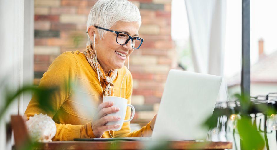 Woman looking at laptop with headphones in while drinking coffee